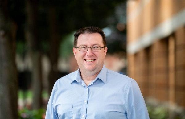 Neal Buckwalter portrait taken outside, he is wearing a blue shirt